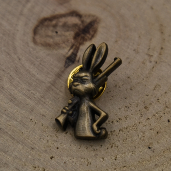 Przypinka myśliwska - zając ze strzelbą  na tle drewna